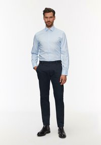 Lichtblauwe button-up blouse met lange mouwen, gecombineerd met donkere broeken en zwarte chelsea boots. Smooth stof en op maat gemaakte pasvorm.