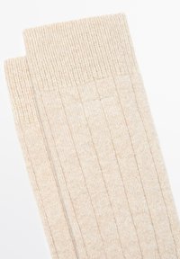 Beige gerippte Socken mit strukturierter Oberfläche und umgeschlagenem Bündchen. Das Material wirkt weich und leicht glänzend und zeigt vertikale Muster.