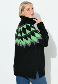 Černý svetr s zelenošedým geometrickým vzorem na ramenou, vysokým límcem a bočními rozparky, vyrobený z měkké pleteniny.