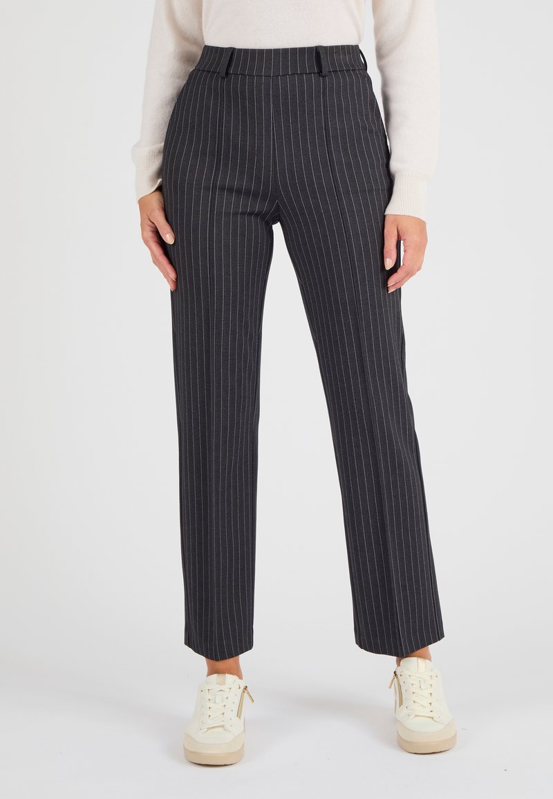 Donkergrijze gestreepte broek met een getailleerde pasvorm, hoge taille en rechte pijpen. De stof heeft een gladde textuur. Gecombineerd met lichte sneakers.