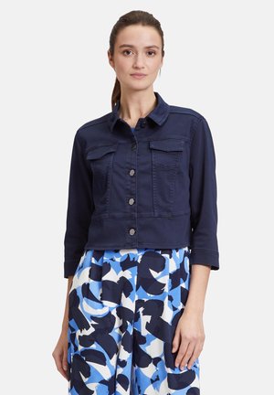 Navy denim cropped jacket with a collar, button closure, and two front pockets, paired with a patterned blue and white skirt.