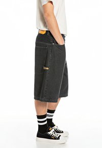 Black denim shorts with a straight design, side pockets, and stitching accents. Paired with black sneakers and striped socks.