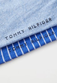 To stk stofprøver: lyseblå med tekstur, sort "TOMMY HILFIGER" branding, og et stribet blåt mønster med hvide striber og matchende branding.