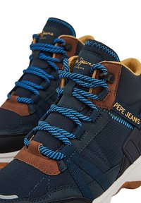 Zapatillas azul y marino oscuro con acentos marrones, material texturizado, cordones azules y suela blanca en contraste. Logotipo "Pepe Jeans" en el lateral.