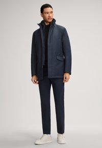 Marine waterdichte jas met hoge kraag, zijzakken en een soepele textuur; gecombineerd met bijpassende broek en witte sneakers.