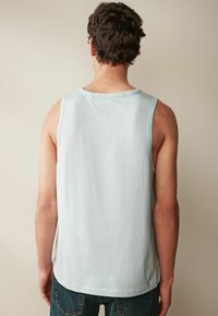 Ljust blå ärmlös skjorta med rund halsringning, mjukt tyg och avslappnad passform, kombinerad med mörka denimjeans.