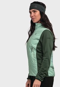 Leichtgewichtige fleece Jacke in Mintgrün mit dunkelgrünen Akzenten, gesteppter Textur auf der Vorderseite und einer seitlichen Reißverschlusstasche. Veredelt mit einem hohen Kragen.