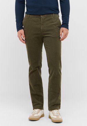 Olivgrüne Cordhosen mit weitem Schnitt, ausgestattet mit einem Knopfverschluss und Gürtelschlaufen, kombiniert mit cremefarbenen und braunen Sneakers.