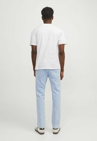 Witte katoenen T-shirt, korte mouwen, ronde hals, gecombineerd met lichtblauwe denimjeans en sandalen. Getextureerde stof, ontspannen pasvorm, minimale details.