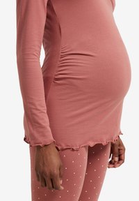 Maternity top in muted pink, soft fabric with curved hem and ruffled edges, paired with coordinating polka dot leggings in matching color.