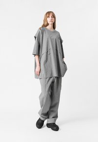 Camiseta gris de gran tamaño con mangas cortas, que presenta un cuello redondeado y un detalle de capas, combinada con pantalones de chándal gris a juego y calzado negro.