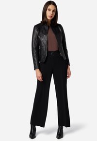 Giacca di pelle nera con un design aderente, top marrone sotto e pantaloni neri a vita alta. Accenti testurizzati sulle spalle.