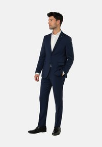 Marineblauer Anzug aus glattem Stoff, mit Reverskragen, Ein-Knopf-Verschluss und schmal geschnittenen Hosen, kombiniert mit einem weißen Hemd.