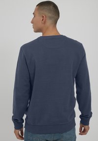 Felpa blu navy con maniche lunghe, scollatura tonda e polsini a costine. Realizzata in tessuto morbido, con una texture liscia.