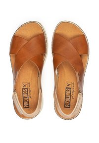 Sandalias de cuero marrón con diseño de tiras entrelazadas en la parte superior, plantilla acolchada y acentos beige. Presenta un borde trenzado y una plantilla con el logo de la marca en relieve.