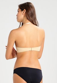Bikini s nahou bandeau horní částí a černými kalhotkami, s klipsovým zapínáním na zádech a hladkým, pružným materiálem.