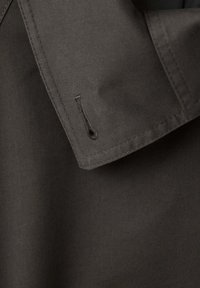 Gros plan sur un tissu sombre avec une boutonnière cousue sur un bord plié, montrant la texture et les détails de la couture.