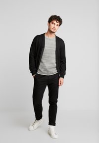 Black cardigan over a gray horizontal striped sweater, paired with black pants and white sneakers. The outfit features a casual fit.