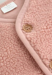 Rózsaszín fleece dzseki, puha, texturált anyagból, sima gallérral és fa gomb díszítéssel. A címke felirata: "NEXT baby."