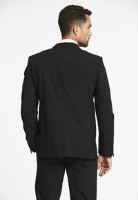 Schwarze Anzugjacke mit einem Schlitze, taillierte Passform und strukturierten Schultern. Sie verfügt über klassische Revers und einen Zwei-Knopf-Verschluss.