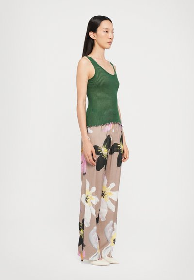 Grünes, geripptes Tanktop kombiniert mit floralen, weit geschnittenen Hosen, die große weiße und rosafarbene Blumenmuster auf einem gedeckten Hintergrund zeigen.