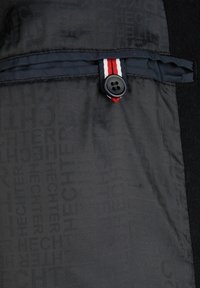 Svart tyg med präglat logomönster. Inkluderar en röd, vit och blå accentrand samt en svart knapp för fickans stängning.