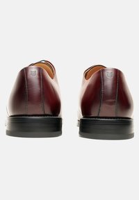 Leren schoenen in donker bordeaux met een gladde textuur, ronde achterkant en een contrasterende zwarte rubberen zool. Minimale branding bij de hak.