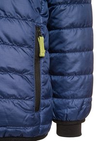 Section de veste matelassée bleu marine avec une poche zippée diagonale dotée d'un curseur vert, un bord contrastant noir et une texture matelassée.