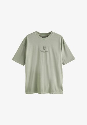 Šviesiai žalia medvilninė marškinėliai su apvalia iškirpte, trumpomis rankovėmis ir priekyje esančiu logotipu su Guinness arfa ir tekstu. Minkšta tekstūra, laisvas kirpimas.