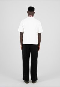 Valge l�ühikese varrukaga särk lillemustritega kraega, koos mustade laia varruka-pükstega ja tumedate kingadega, nähtud tagant.