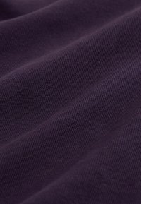 Nahaufnahme eines dunkelvioletten, gerippten Stoffes, der Textur und Strickmuster mit sanften Falten und weichem Licht zeigt.