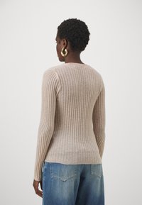 Beige ribbstickad tröja med långa ärmar, tajt passform och rund halsringning, kombinerad med blå vida jeans. Mjuk textur, minimala detaljer.