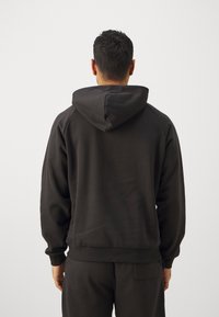 Hanorac negru cu glugă, fabricat dintr-un material moale, cu un croi lejer, mâneci raglan și manșete ribbate, văzut din spate.