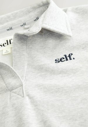 Harmaa polo-paita, joka on valmistettu pehmeästä kankaasta. Paitassa on kauluspääntie ja pieni tummansinisestä langasta brodeerattu logo "self." rinnassa.