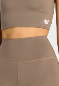 Brązowy zestaw sportowy składający się z krótkiego topu i legginsów z wysokim stanem. Wykonany z gładkiego, elastycznego materiału z subtelnymi detalami szwów.