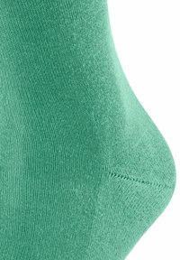 Groene sok met een zachte gebreide textuur. Beschikt over een taps toelopende vorm en een versterkte teen, met complexe stiksels en een gladde afwerking.