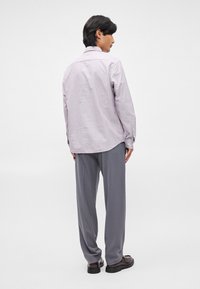 Ljust lila randig skjorta med klassisk krage och knäppningar vid ärmarna. Kombinerad med lösa grå byxor och svarta skor. Bakifrån.