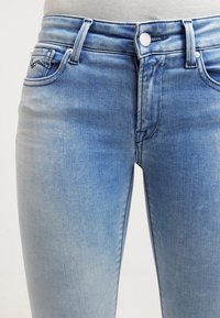 Jeans de mezclilla azul claro con un aspecto desgastado, diseño de cinco bolsillos, cierre de botón y detalles de costura sutiles en la cinturilla.