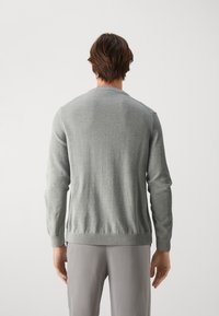 Pull en maille grise à manches longues, col rond et poignets côtelés. Présente une texture lisse et une coupe ajustée, vu de dos.