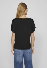 Top corto nero a maniche corte con vestibilità ampia, scollatura rotonda e texture liscia. Abbinato a jeans larghi blu chiaro.