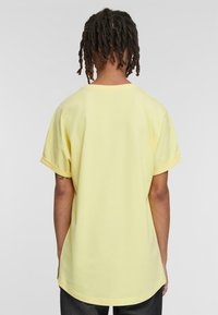 Camiseta corta amarilla de manga corta con cuello redondo, corte relajado y puños enrollados. Tejido de algodón suave con una textura lisa.