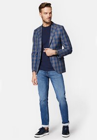Niebieska marynarka w kratę na granatowej koszulce, w zestawieniu z jasnoniebieskimi dżinsami i granatowymi trampkami. Marynarka ma klapy w kształcie łezki i dwa guziki.