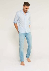 Camisa de cuadros en azul claro con botones combinada con jeans azules claros. La camisa tiene mangas largas y los jeans son ajustados con un ligero desgaste.
