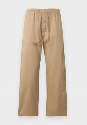 Hellbraune locker sitzende Hose mit elastischem Bund und vorne mit Kordelzug, aus leichtem Stoff, vor einem einfarbigen Hintergrund gezeigt.