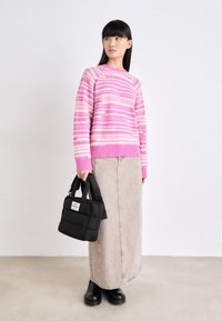 Pull rayé rose et blanc avec un ourlet côtelé, associé à une jupe maxi en denim beige et des bottines noires. Tenant un sac à main noir en forme de coussin.