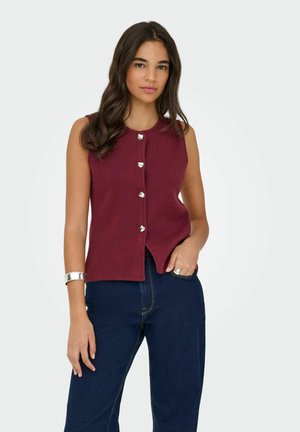 Top sans manches bourgogne avec un col rond et cinq boutons argentés. Le tissu a une texture lisse avec un ourlet droit. Assorti à un jean foncé.