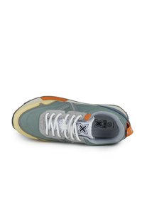 Zapatilla con parte superior gris y verde, ante texturizado y malla, cordones blancos, acento naranja y suela de goma amarilla. Presenta cierre con cordones.