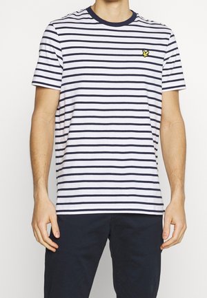 Homme portant un t-shirt blanc à manches courtes avec des rayures horizontales bleu marine et un petit logo d'oiseau jaune sur la poitrine gauche.