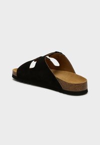 Svart mocka slide sandal med öppen tå, utskärningsdesign på sidan och en ljusbrun korkfotbädd. Mönstrad gummisula för bra grepp.