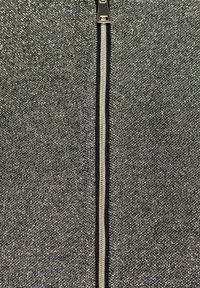 Grijze, gestructureerde stof met een subtiele glans, voorzien van een centrale rits in zilver met een zwarte voering langs de randen.